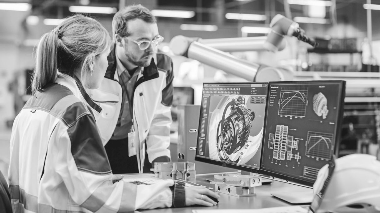 Engineers working on a computer with 3D mechanical design and performance charts displayed on dual monitors in an advanced manufacturing environment. Driving AEC digital transformation